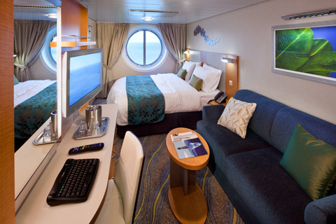 Ocean View Cabin with large porthole window, king bed, sofa, and desk aboard Oasis of the Seas